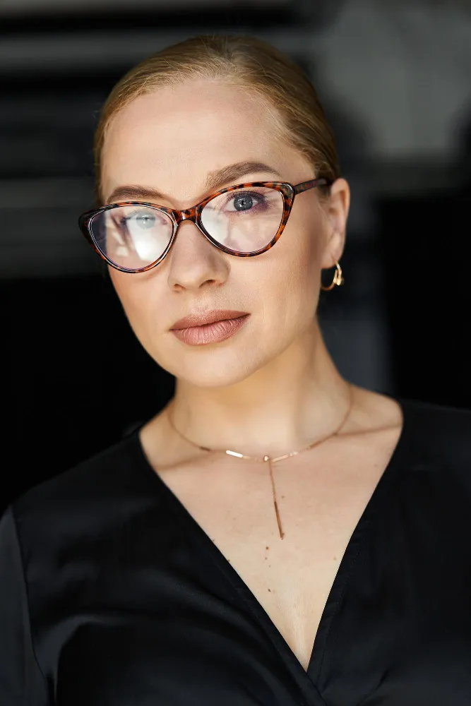 Woman wearing tortoiseshell glasses and black top looking at camera