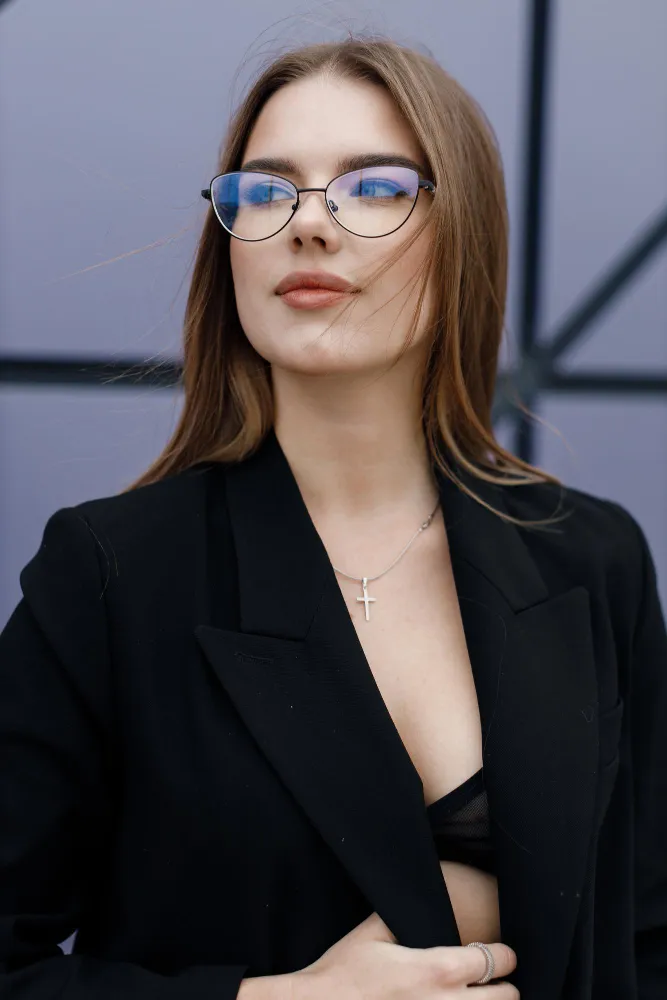 Young woman wearing round glasses and black blazer with cross necklace