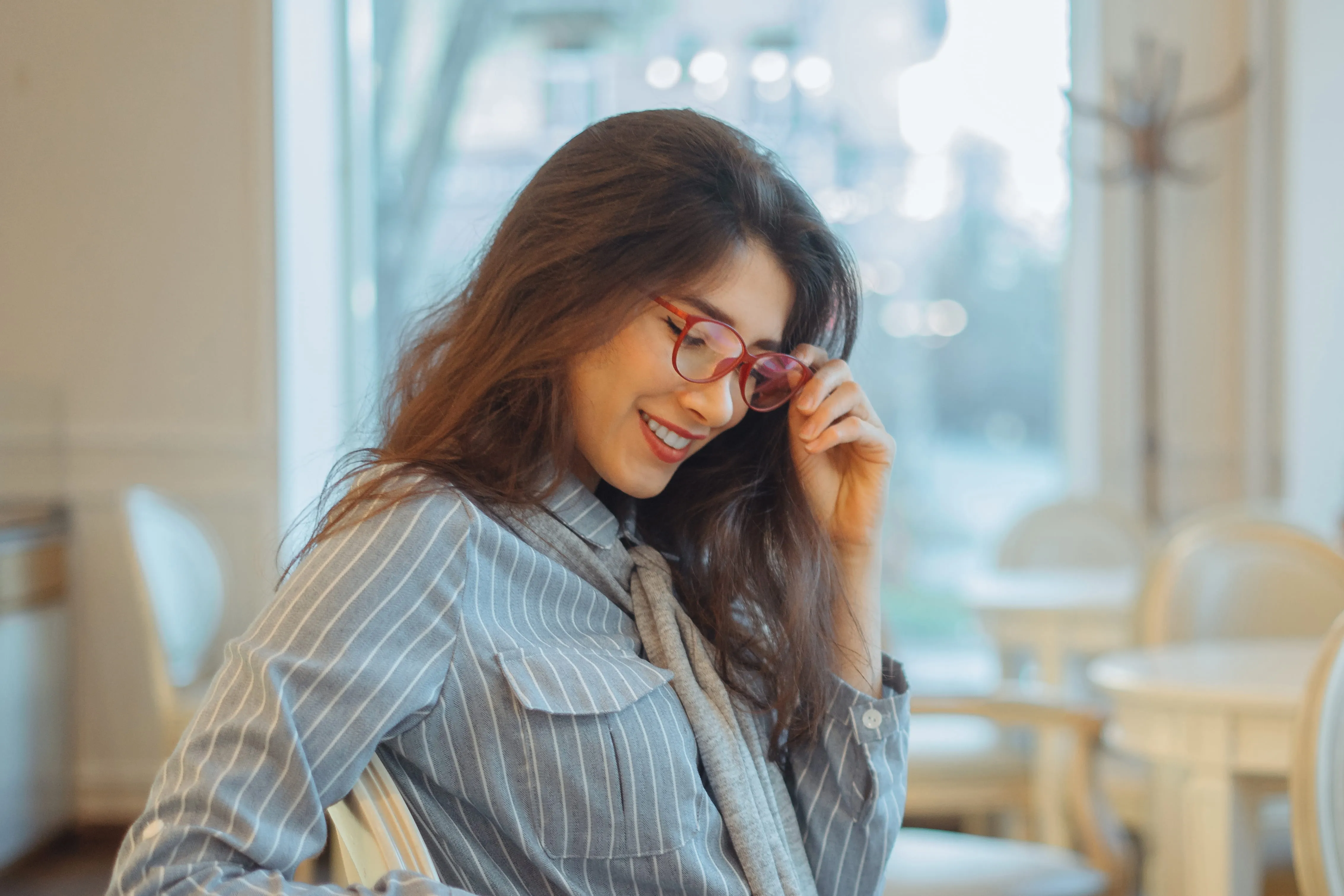 Smiling woman in gray pinstripe suit wearing red glasses in modern office