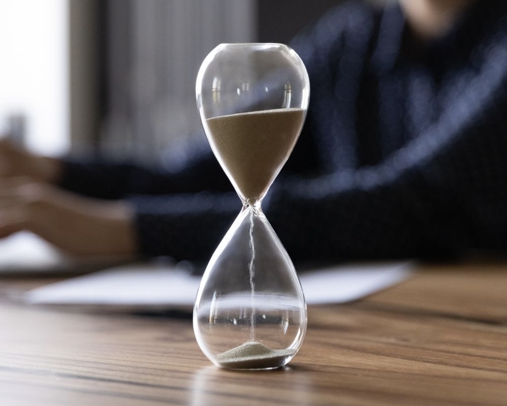 Sablier en verre posé sur une table en bois avec du sable coulant de la partie supérieure à la partie inférieure.