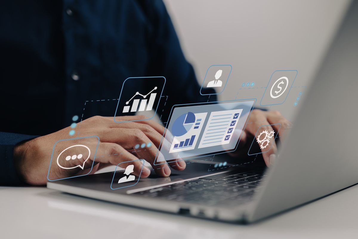 Mains d'une personne tapant sur un ordinateur portable avec des icônes numériques de graphiques et gestion de données flottant au-dessus.