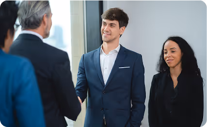 A businessman in a suit and a businesswoman with short grey hair collaborating and writing on a glass whiteboard during a team meeting.
