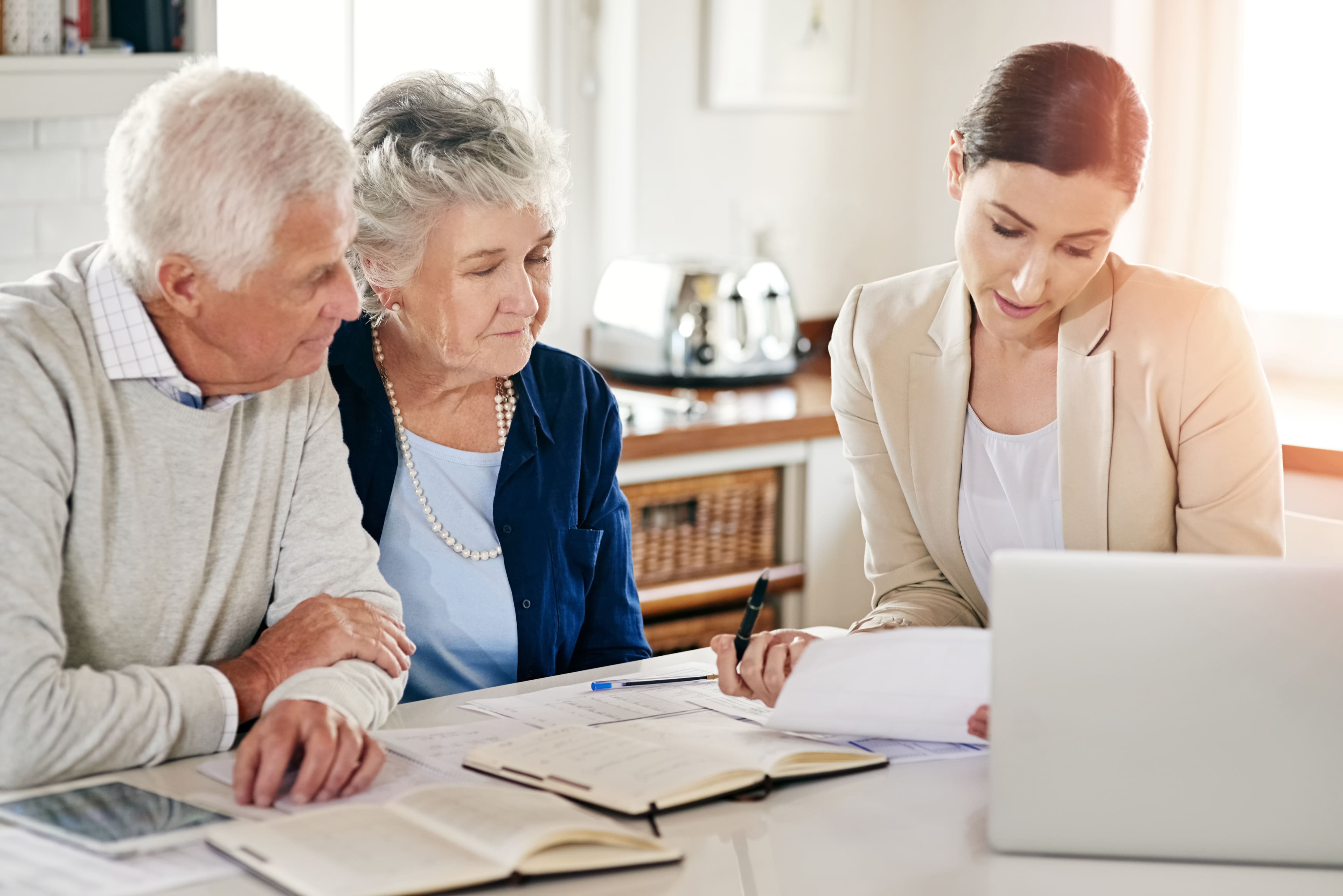 A female advisor or attorney reviewing documents at a table with a senior couple next to an open laptop.