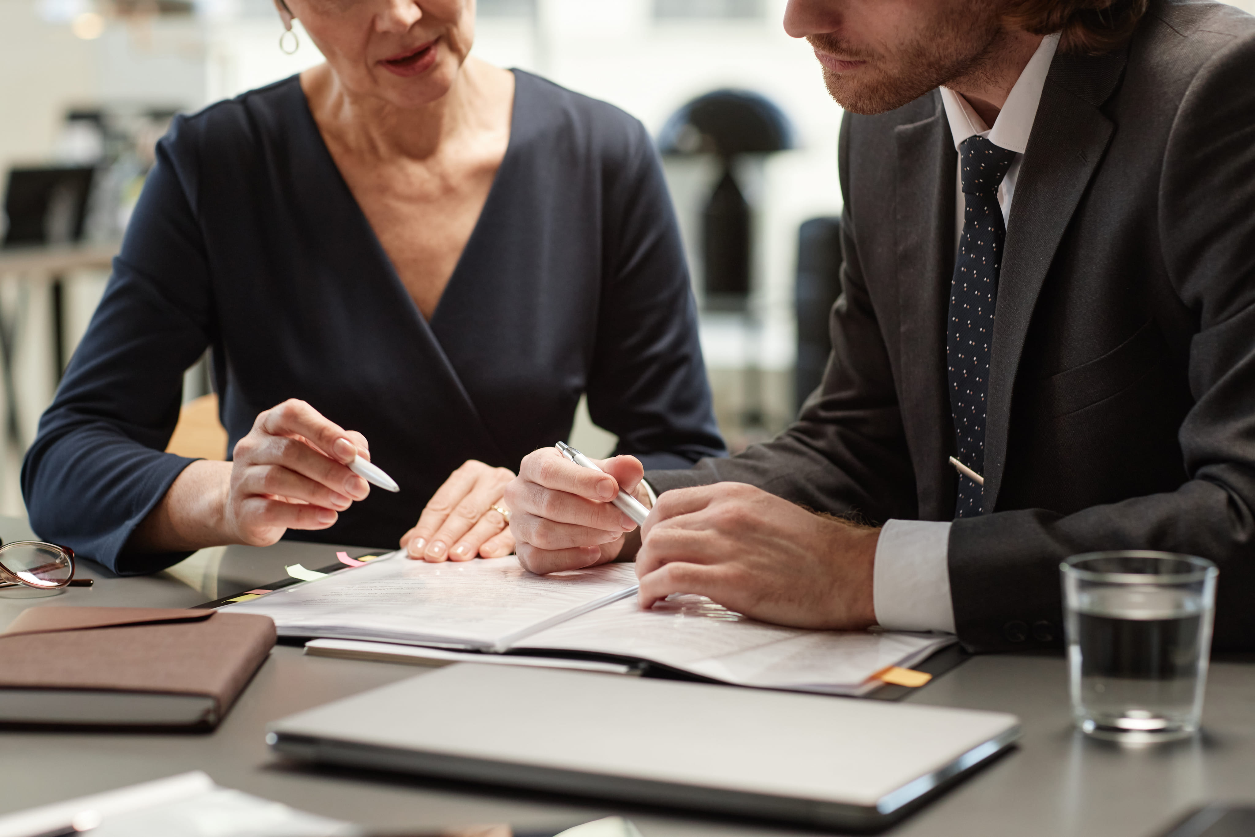 A woman and a male attorney in a suit sitting at a desk together reviewing a folder of legal documents.