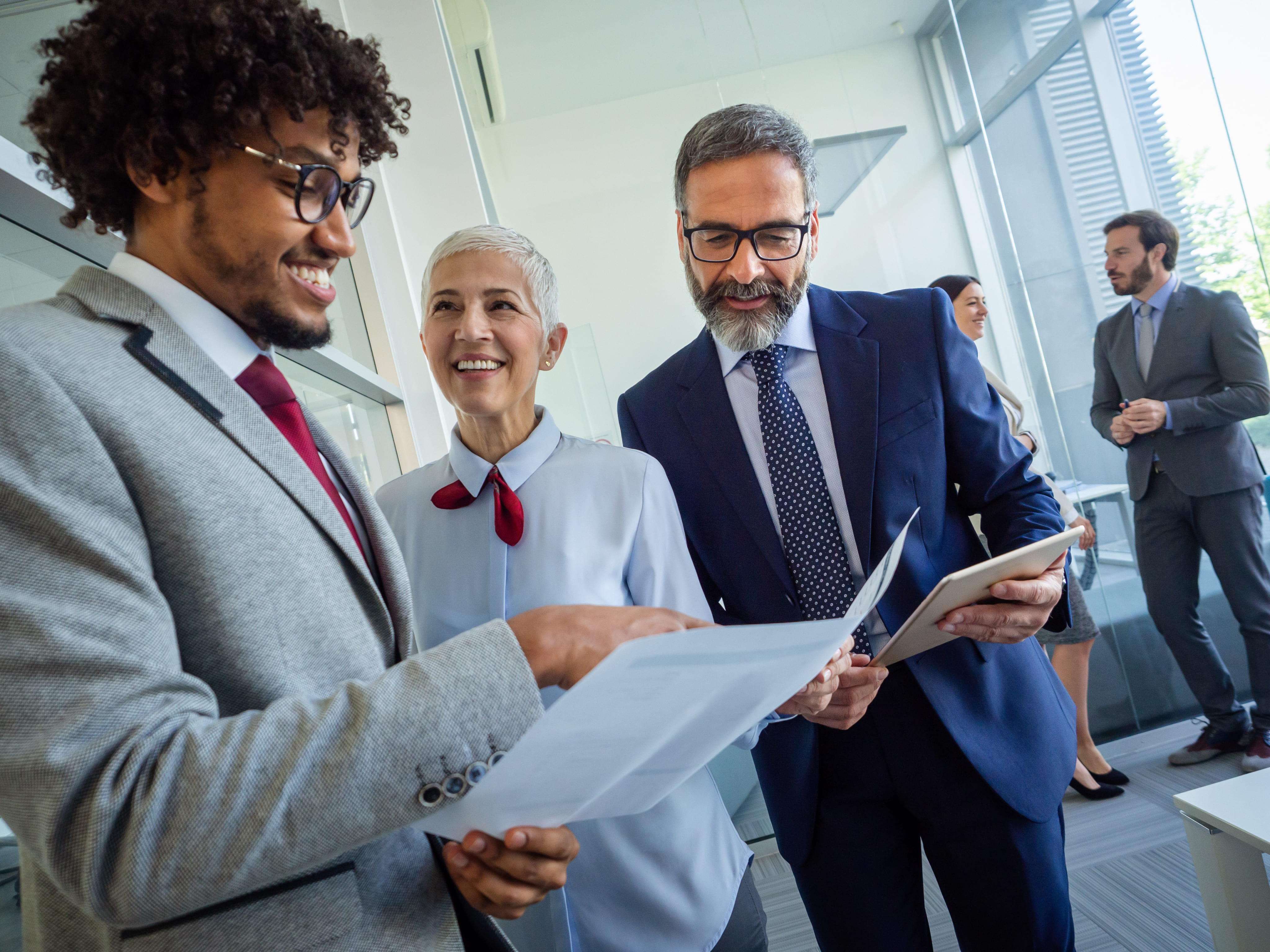 A diverse team of business professionals smiling and reviewing legal or corporate documents together in an office setting.