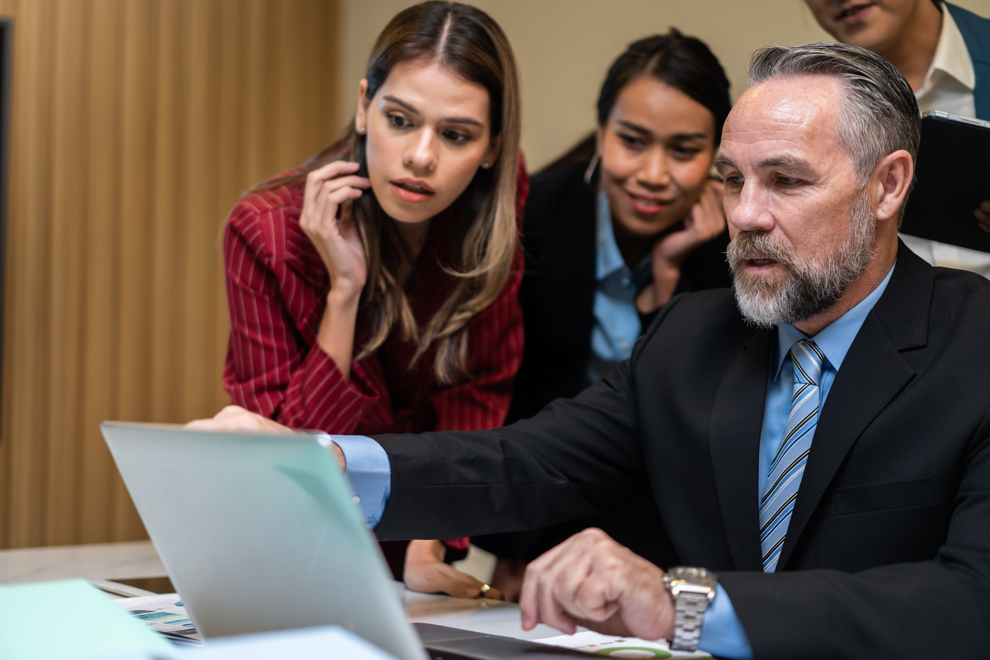 A businessman pointing at a laptop screen while explaining details to two focused female colleagues.