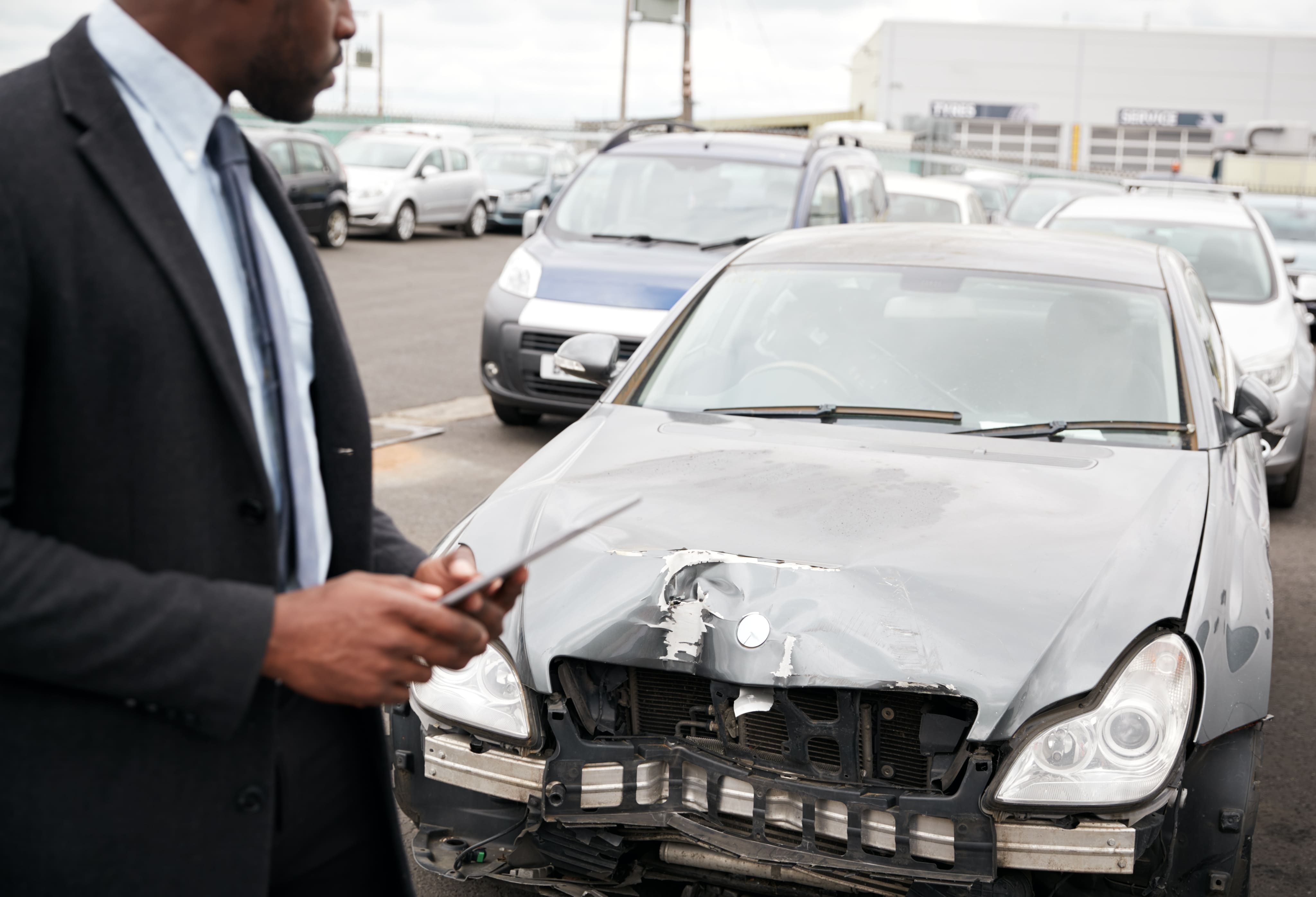 An investigator in a suit evaluating a severely wrecked silver car.