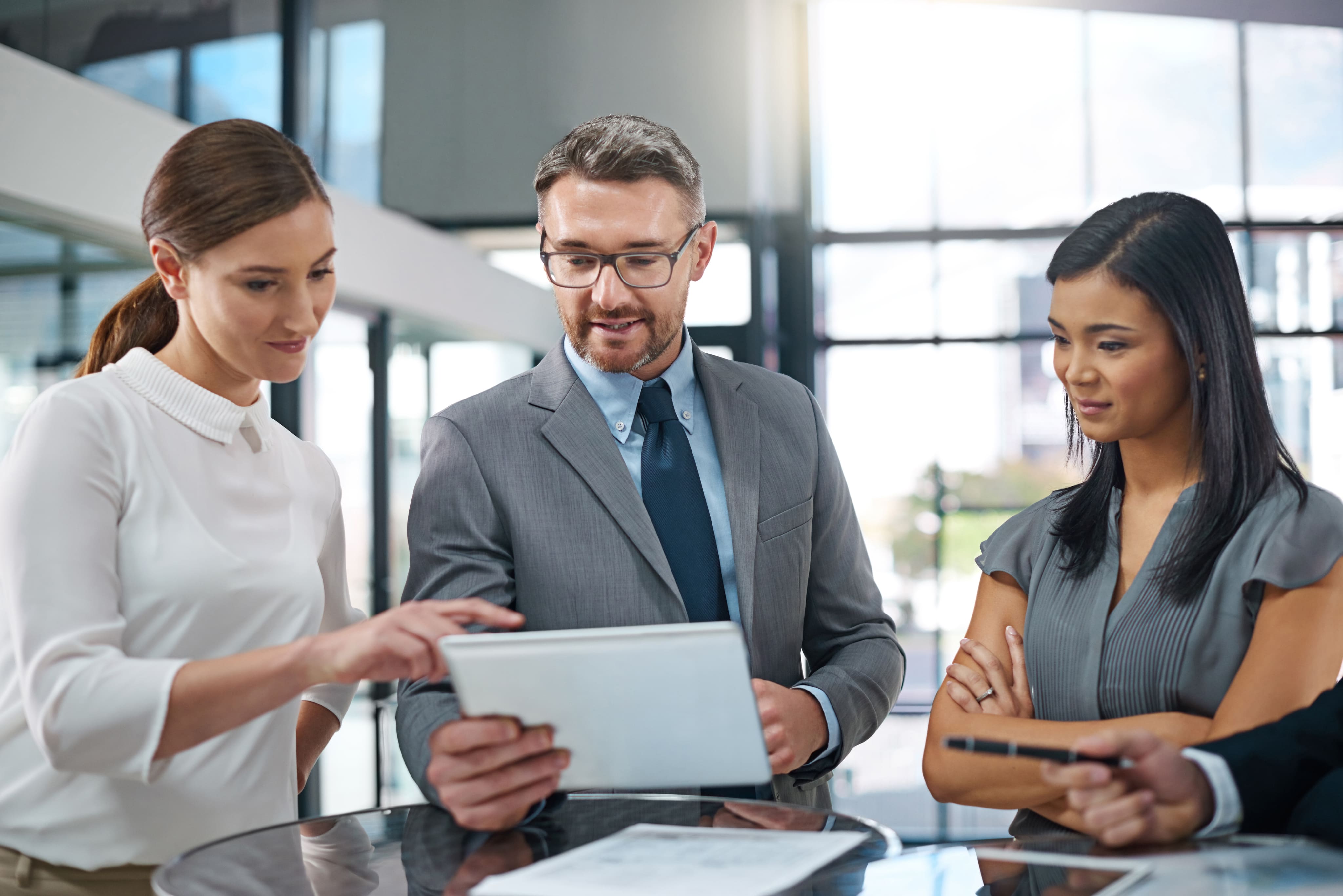Three corporate professionals reviewing data or documents together on a digital tablet in a modern office.