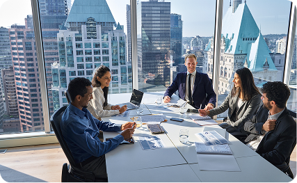 A team of business professionals holding a meeting around a conference table in a high-rise office overlooking a city skyline.