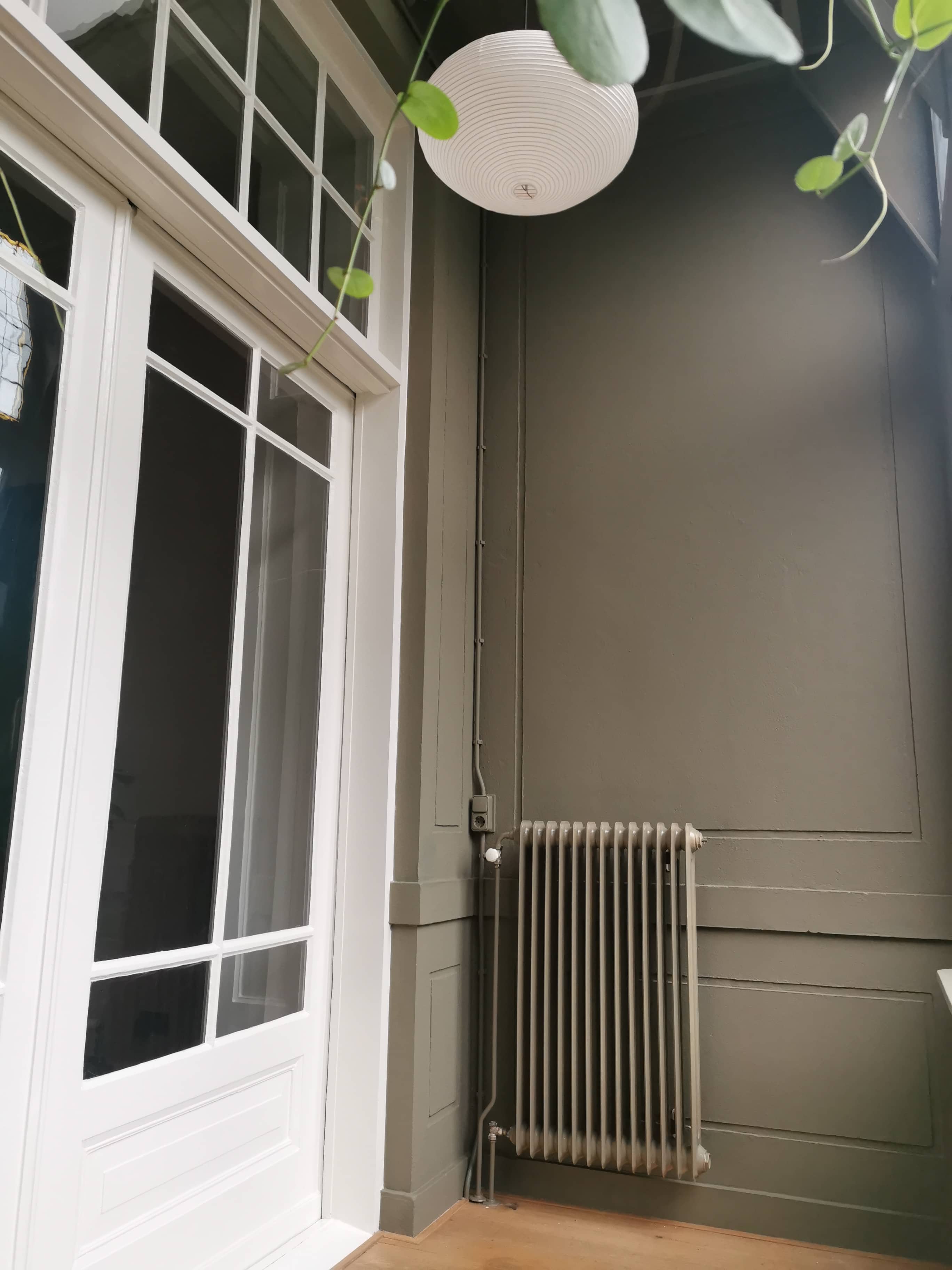 Klassieke binnendeur en raampartij met wit kozijn en grijsgroen geschilderd paneelwerk.