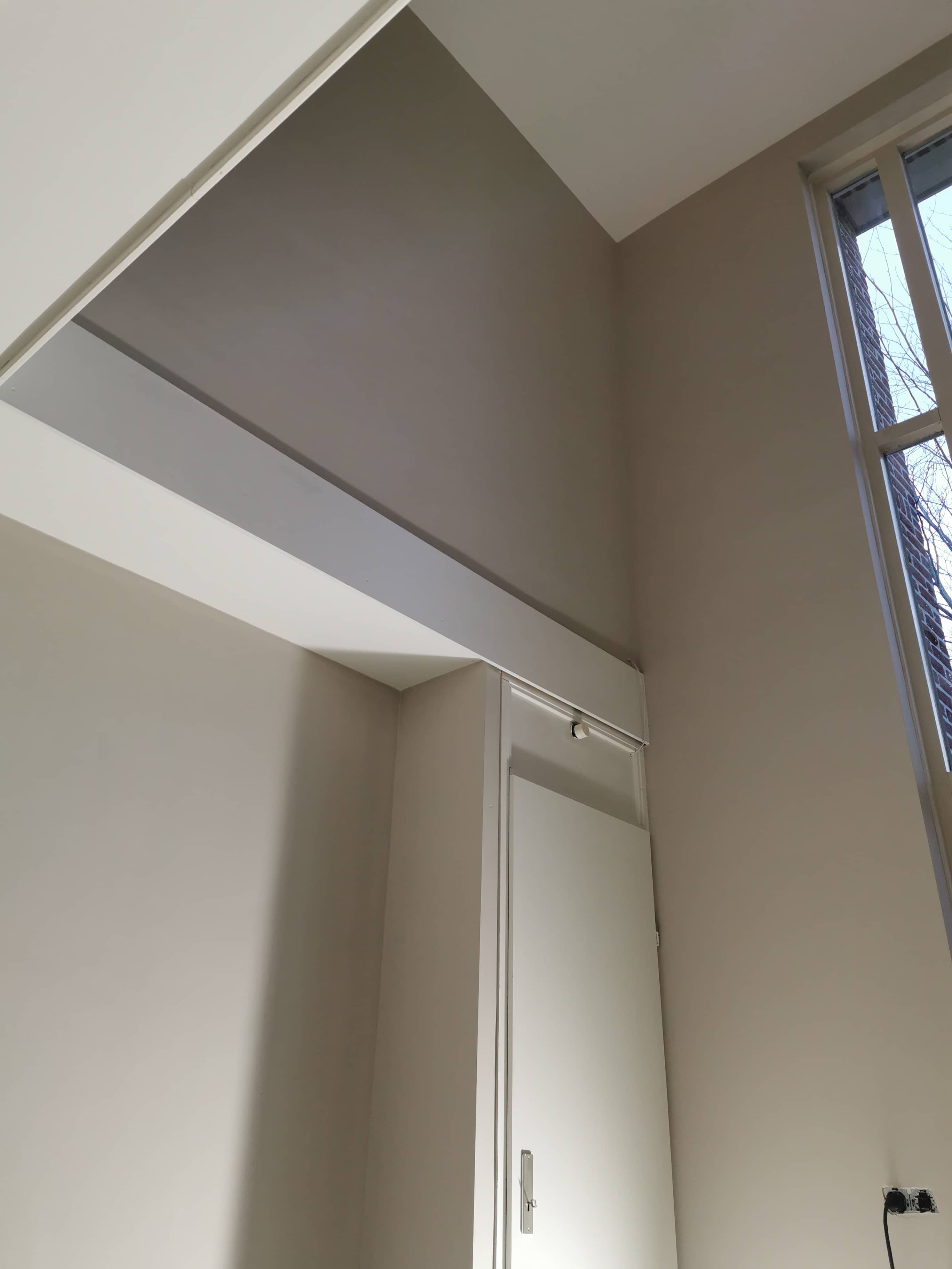 Binnenschilderwerk van een lichte hal met schuin plafond en strakke afwerking van de raamomlijsting en muren.