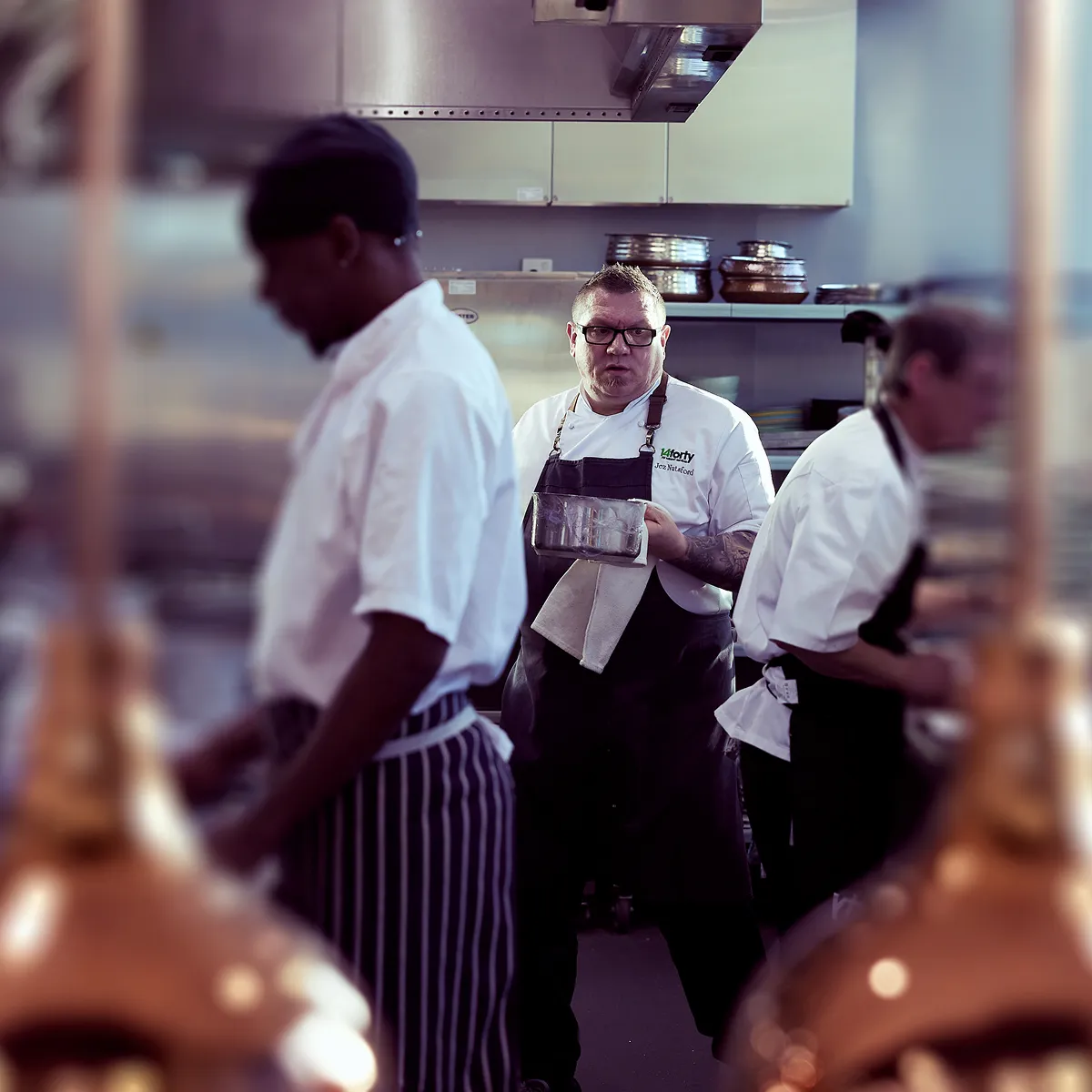 A kitchen setting with 3 men working and 1 of them in clear focus in the middle.