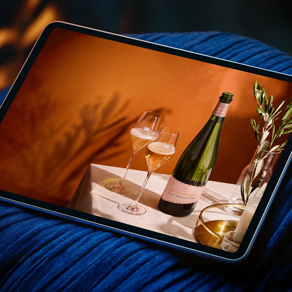 An image of a bottle of Exton Park wine with 2 glasses in a summery background.