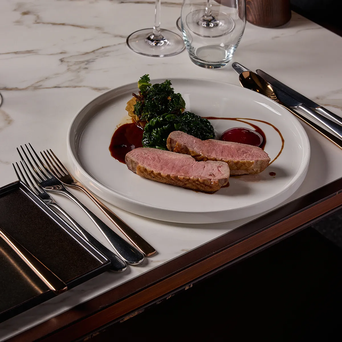 A delicious plate of food with cutlery and glassware on a high end table.