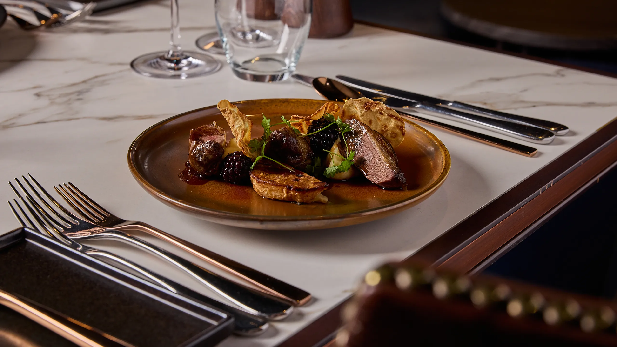 A delicious plate of food with cutlery and glassware on a high end table.