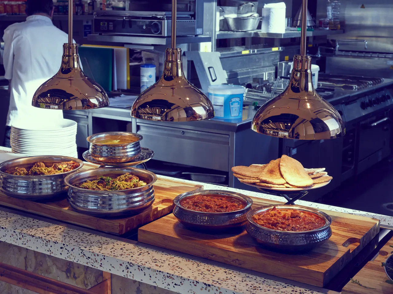 Indian food under hot lights in a high end kitchen in the background.