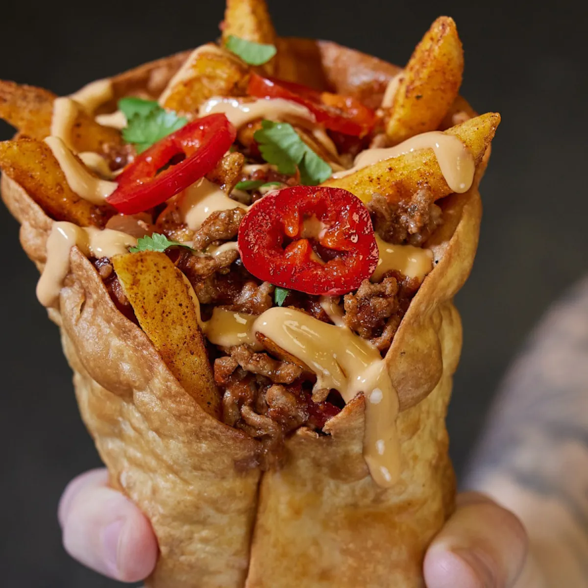 A toasted tortilla filled with chips, meat and sauce with chilli's on top