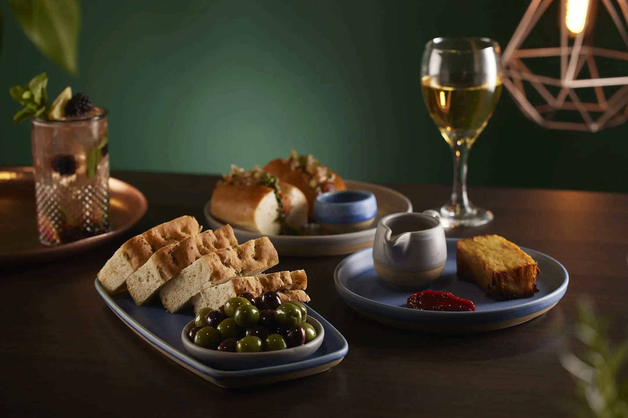 3 plates of food with a glass of wine in front of a green background with a gold lamp.