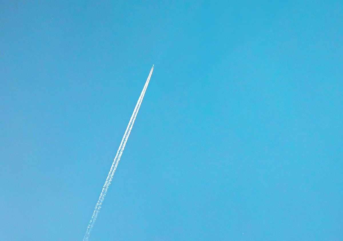 A white airplane contrail cutting diagonally across a clear blue sky