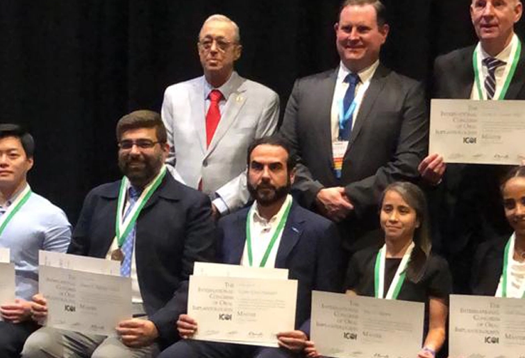 Group of people wearing medals and holding certificates, posing for a photo in front of a black backdrop.