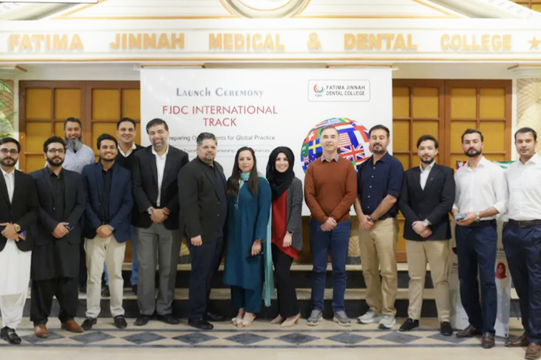 Group of men and women standing indoors in front of a banner that reads 'Launch Ceremony FJDC International Track' at Fatima Jinnah Medical & Dental College.