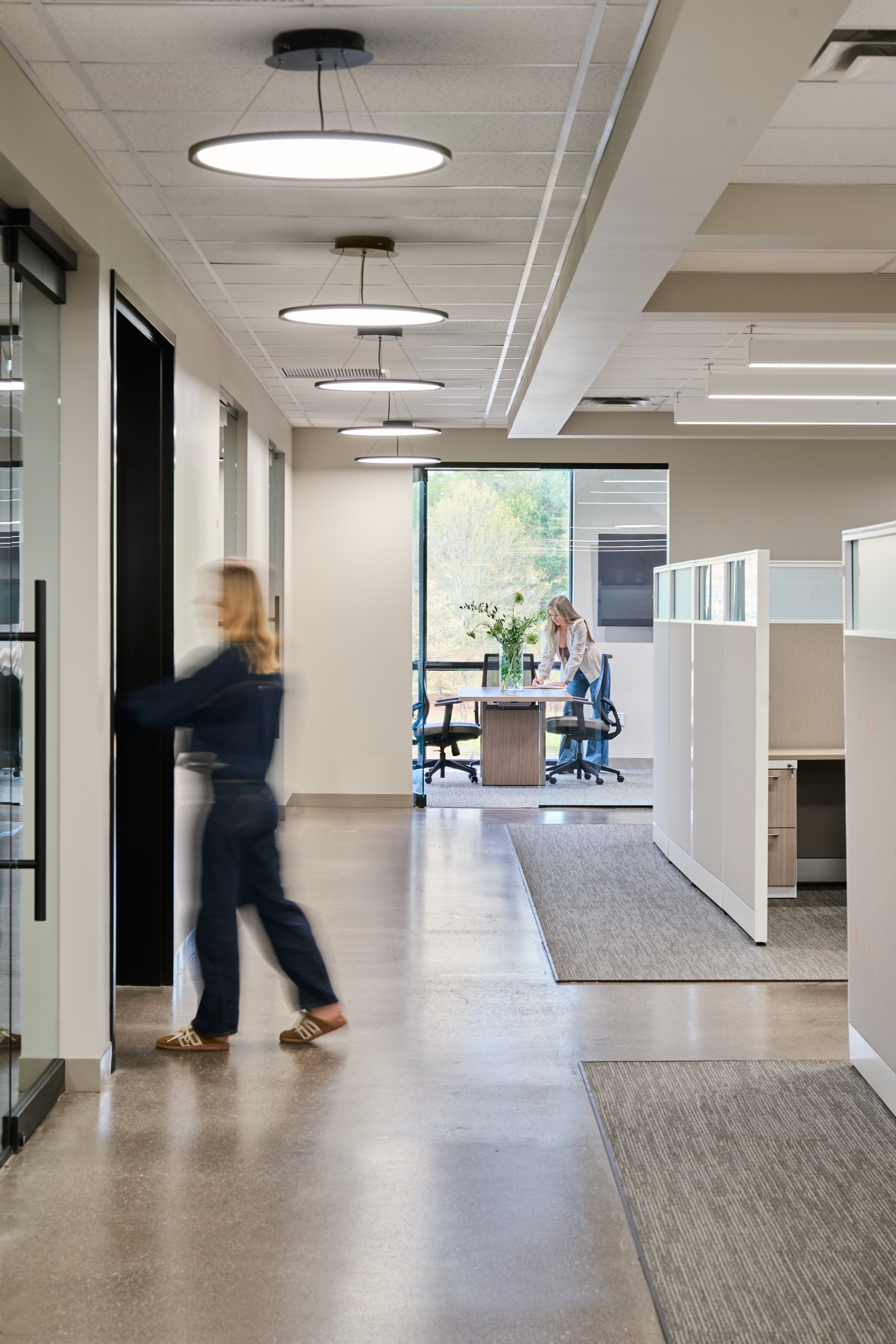 Office corridor under drum pendants leading to a daylit breakout area, workplace photography by Omar Mohammad Studio