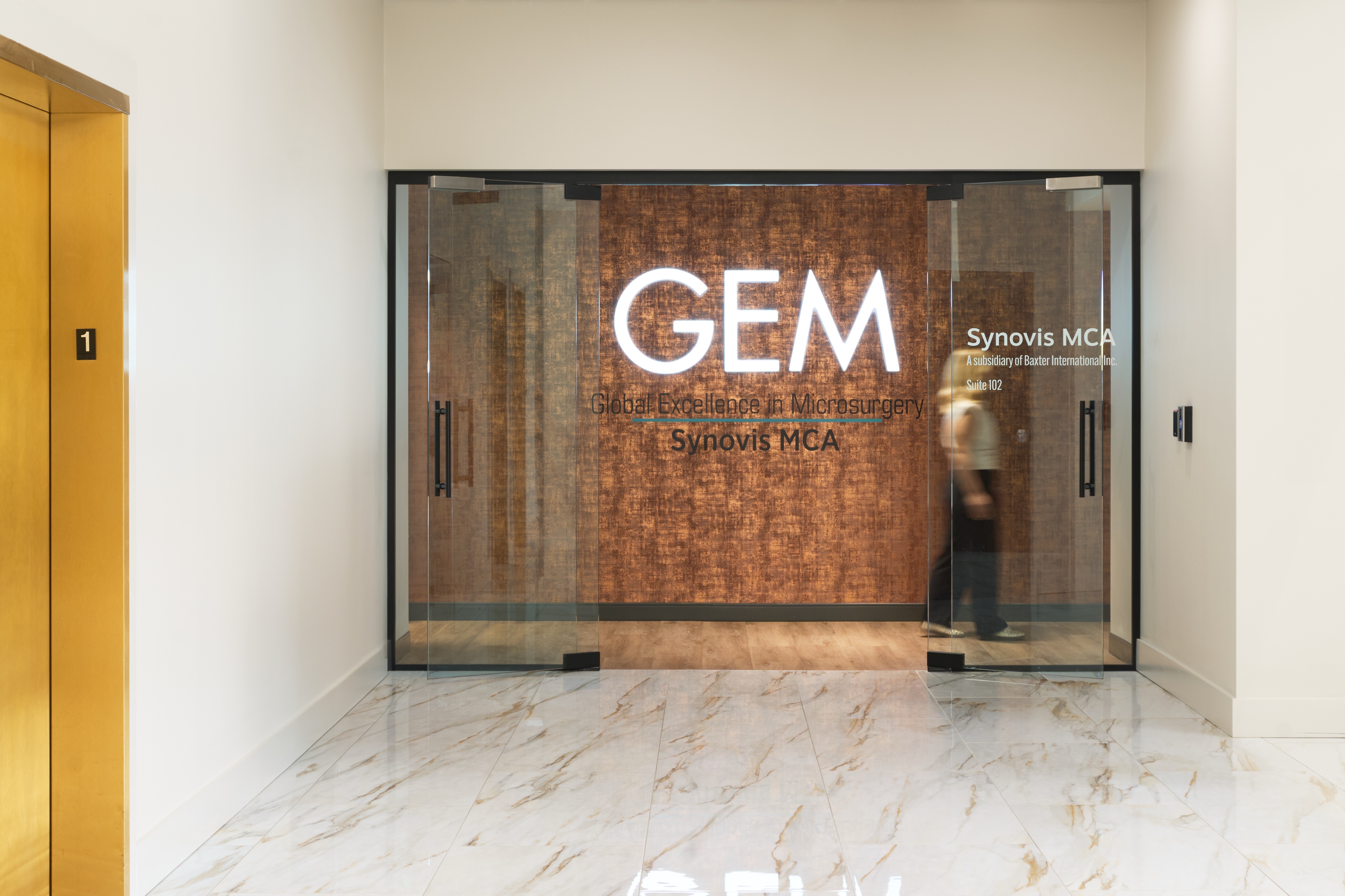 GEM and Synovis MCA entrance with etched glass doors against a patterned wood wall, workplace photography by Omar Mohammad Studio