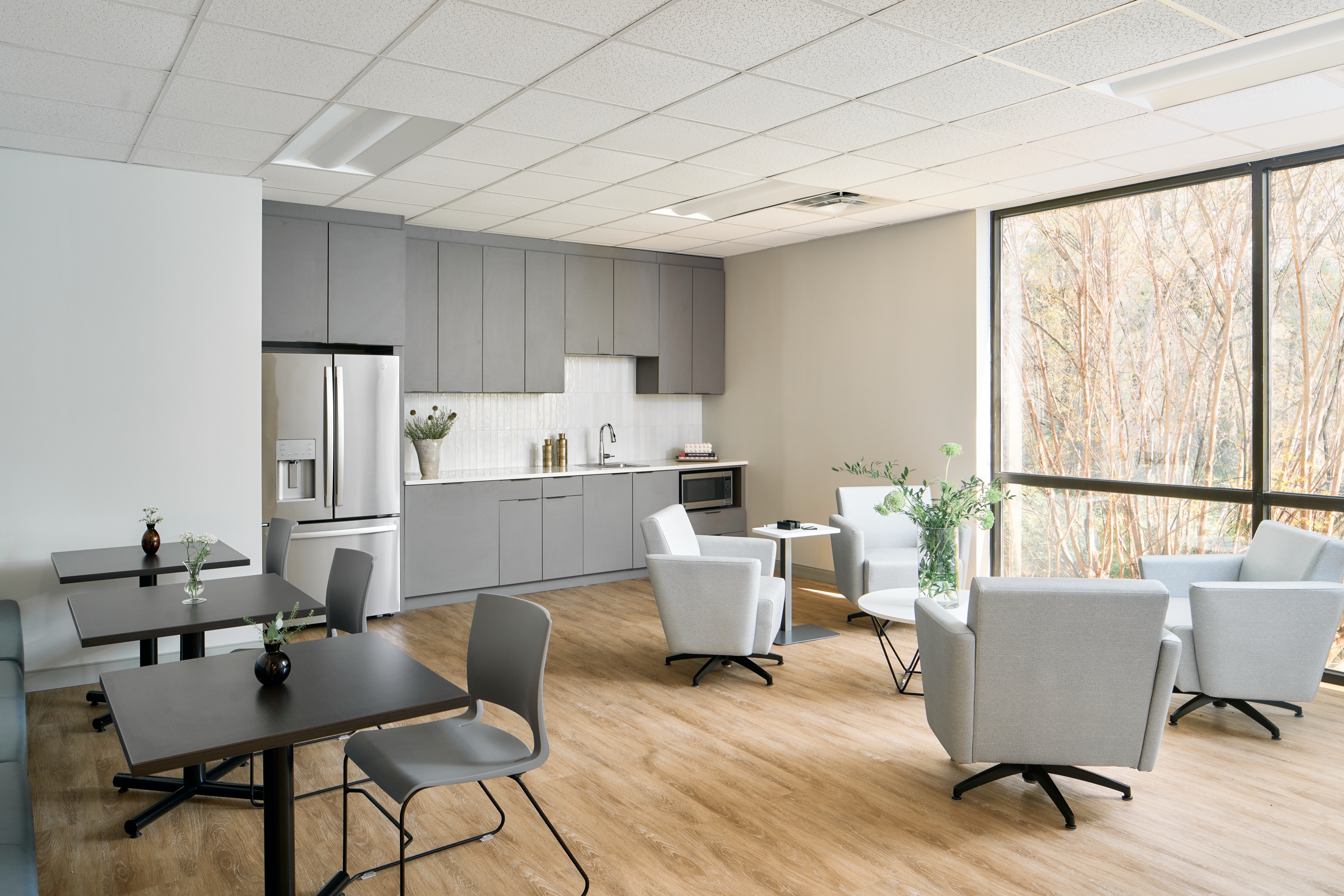 Employee break room with grey kitchen, cafe tables and lounge chairs at a window wall, workplace photography by Omar Mohammad Studio