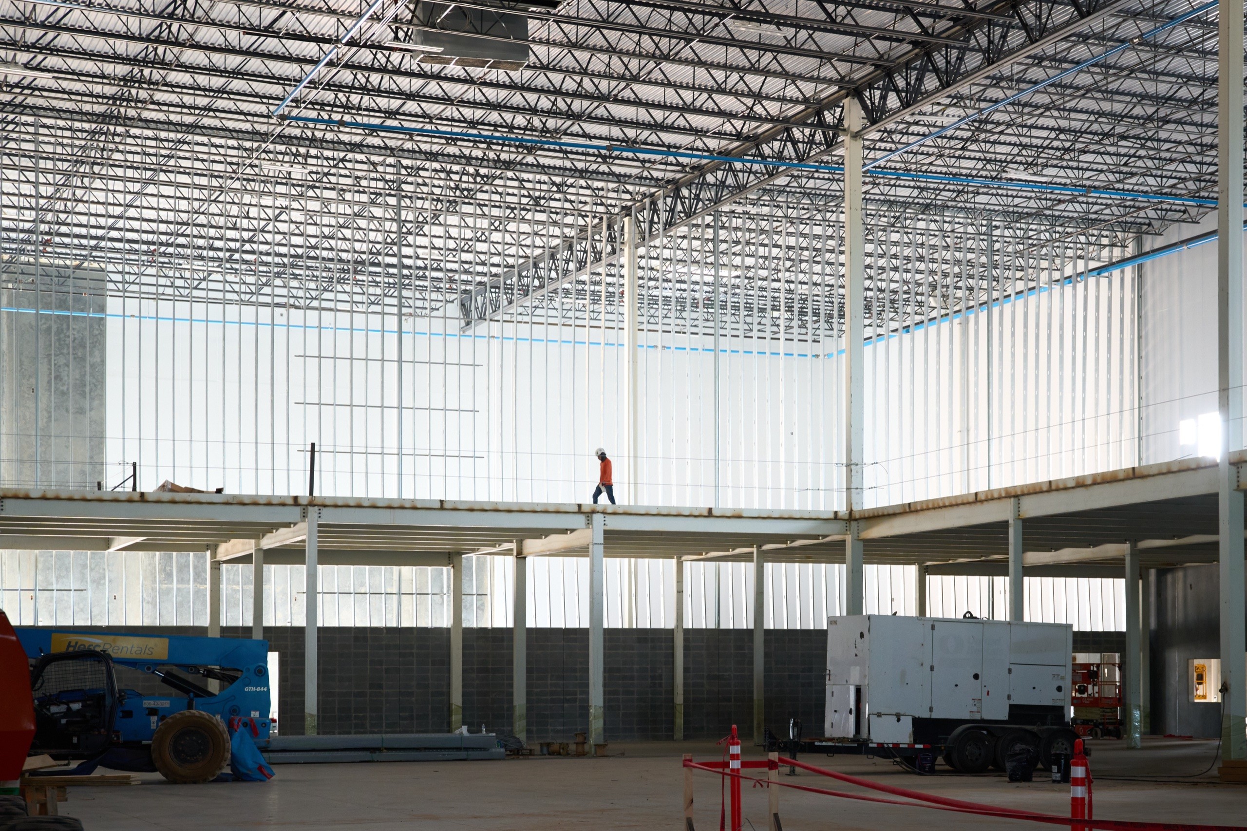 Worker walking a mezzanine beam inside the steel frame at the Statesboro project by Cooper Construction, construction photography by Omar Mohammad Studio
