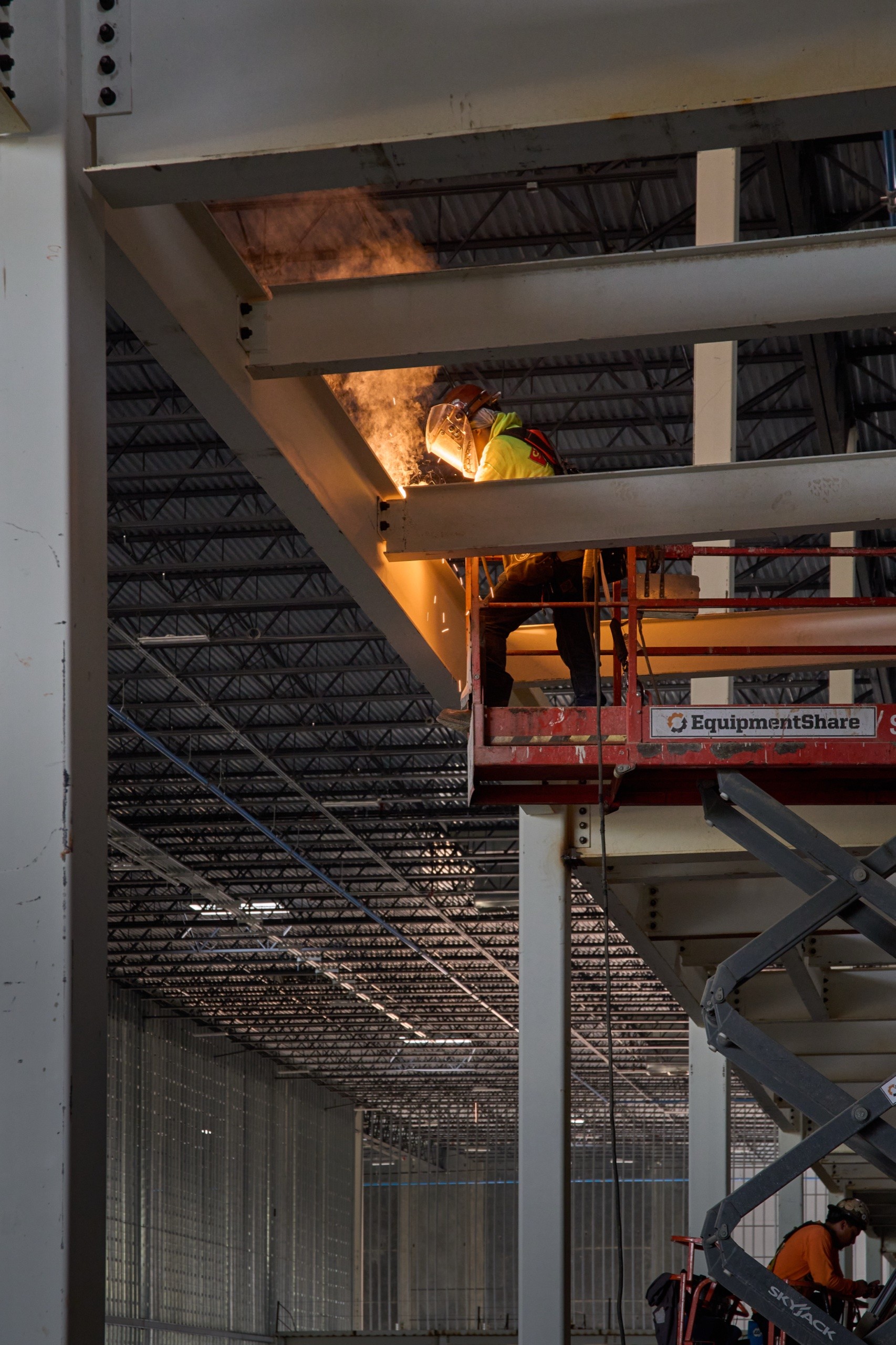 Welder on a lift working a steel beam at the Statesboro project, construction photography by Omar Mohammad Studio