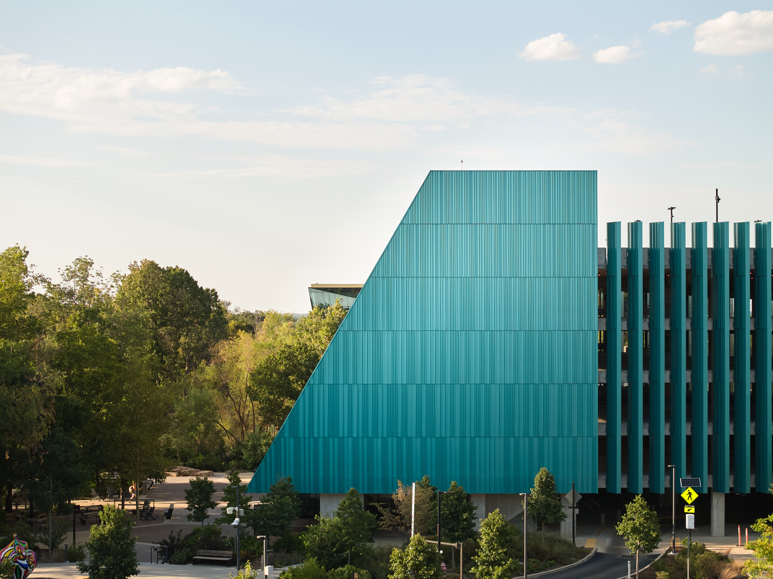 Sloped teal fin facade of the Crystal Bridges parking deck rising above the trees, architectural photography by Omar Mohammad Studio