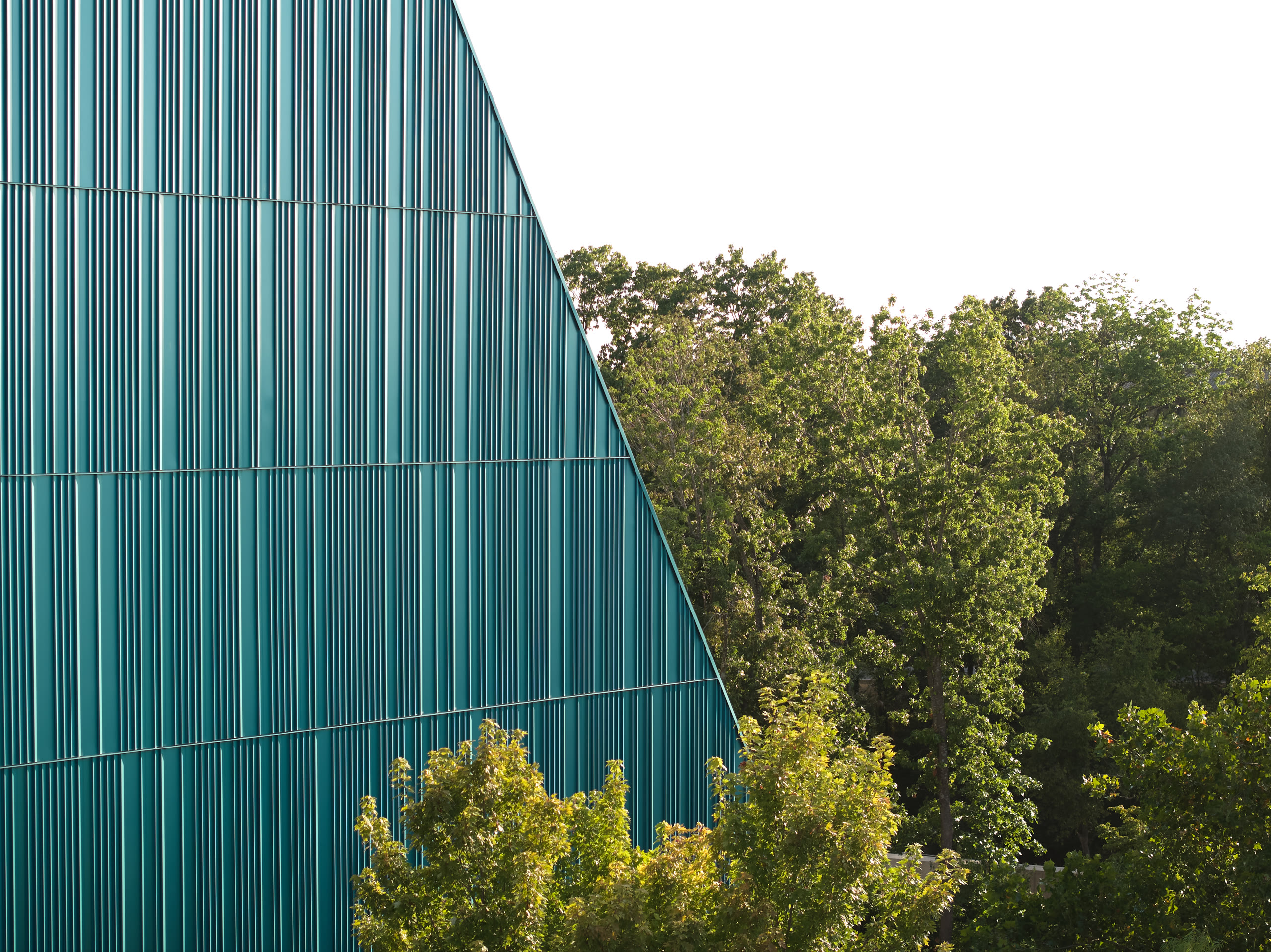 Teal fin wall of the Crystal Bridges parking deck against the treeline, architectural photography by Omar Mohammad Studio