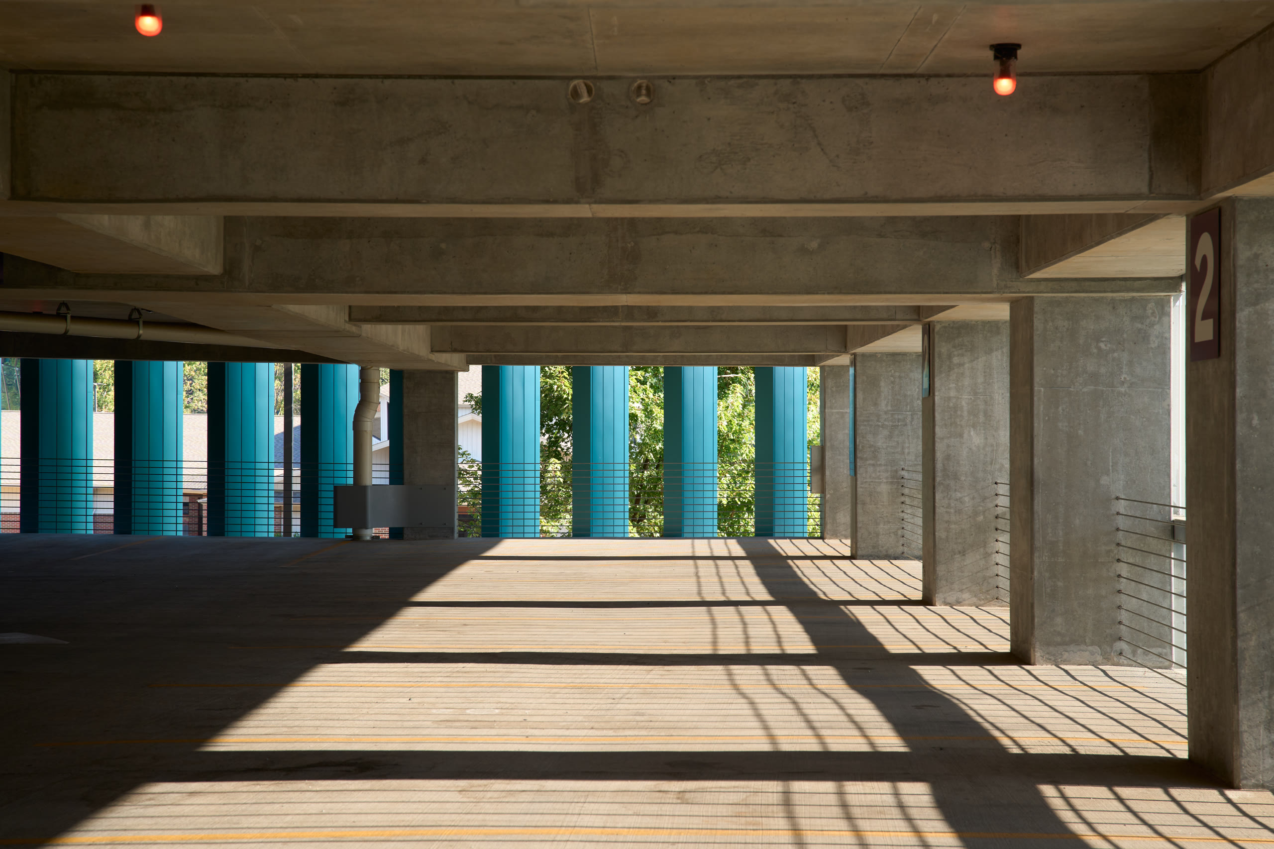Light and shadow across a parking level framed by teal columns at the Crystal Bridges parking deck, architectural photography by Omar Mohammad Studio