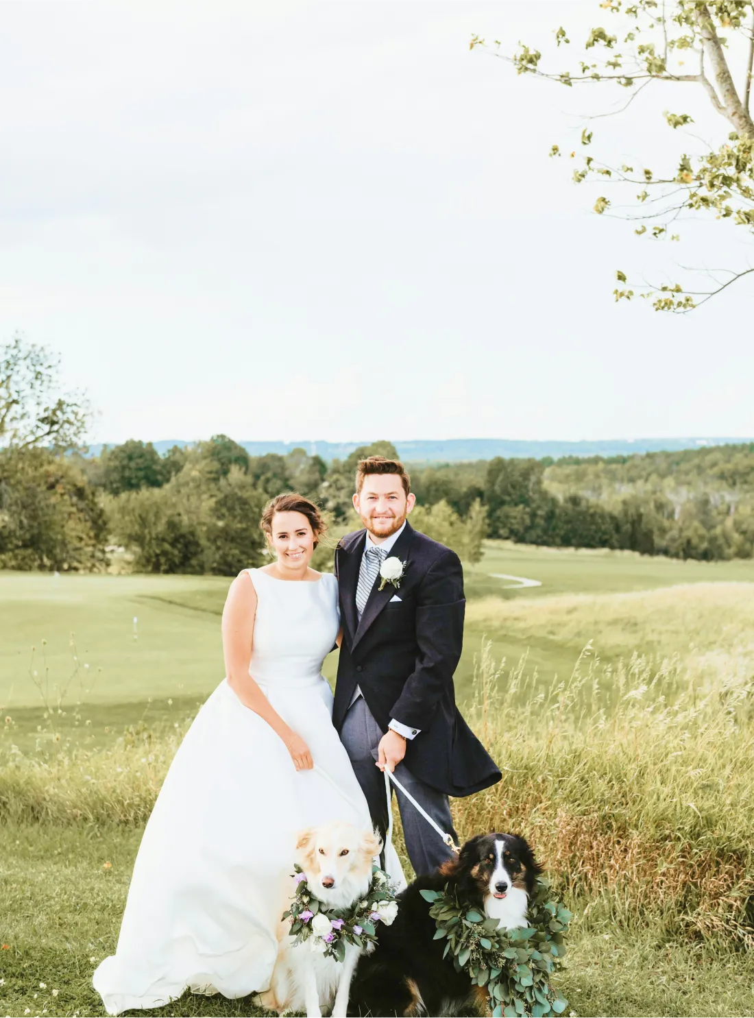 A married couple with dogs in a green valley with trees and flowers