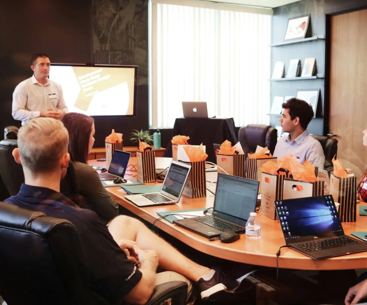 Corporate training session in a modern conference room with presenter and attendees seated around a table