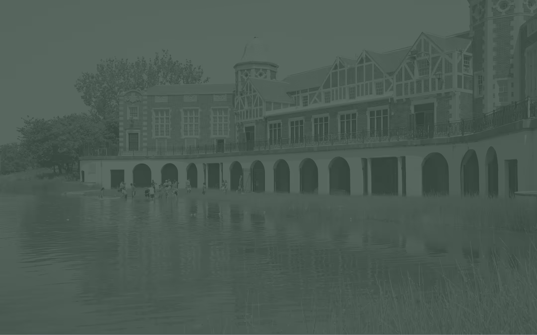 The boat house in Humboldt Park with multiple arched openings along a waterfront where several families are gathered near the water's edge.