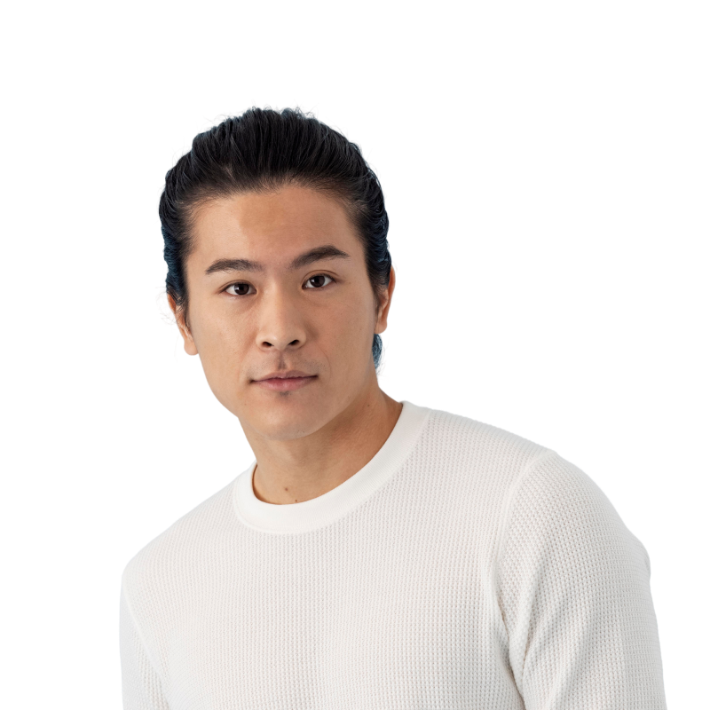 Portrait of a man with dark hair tied back wearing a white textured sweater looking at the camera.