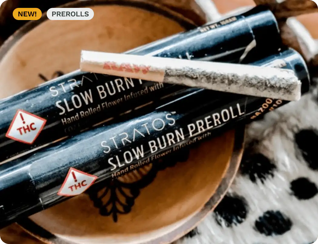 A RAW brand pre-rolled joint resting on black STRATOS Slow Burn Preroll tubes on a wooden surface.