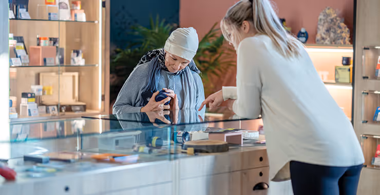 Image of a smiling elderly woman and a young blonde woman looking at the display case in a cannabis shop