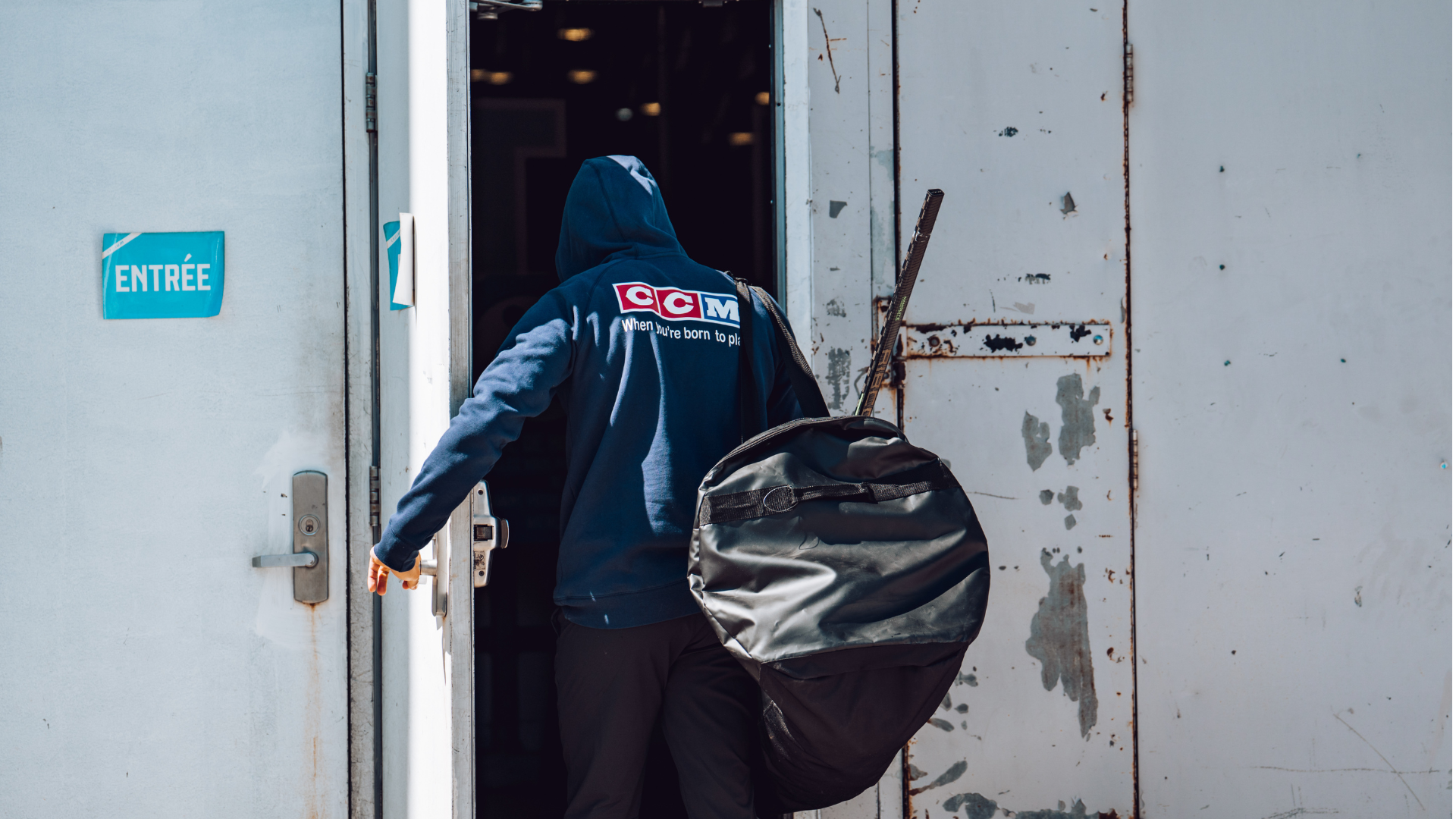 Jääkiekkoilija kävelee ovesta sisään jääkiekokassin kanssa