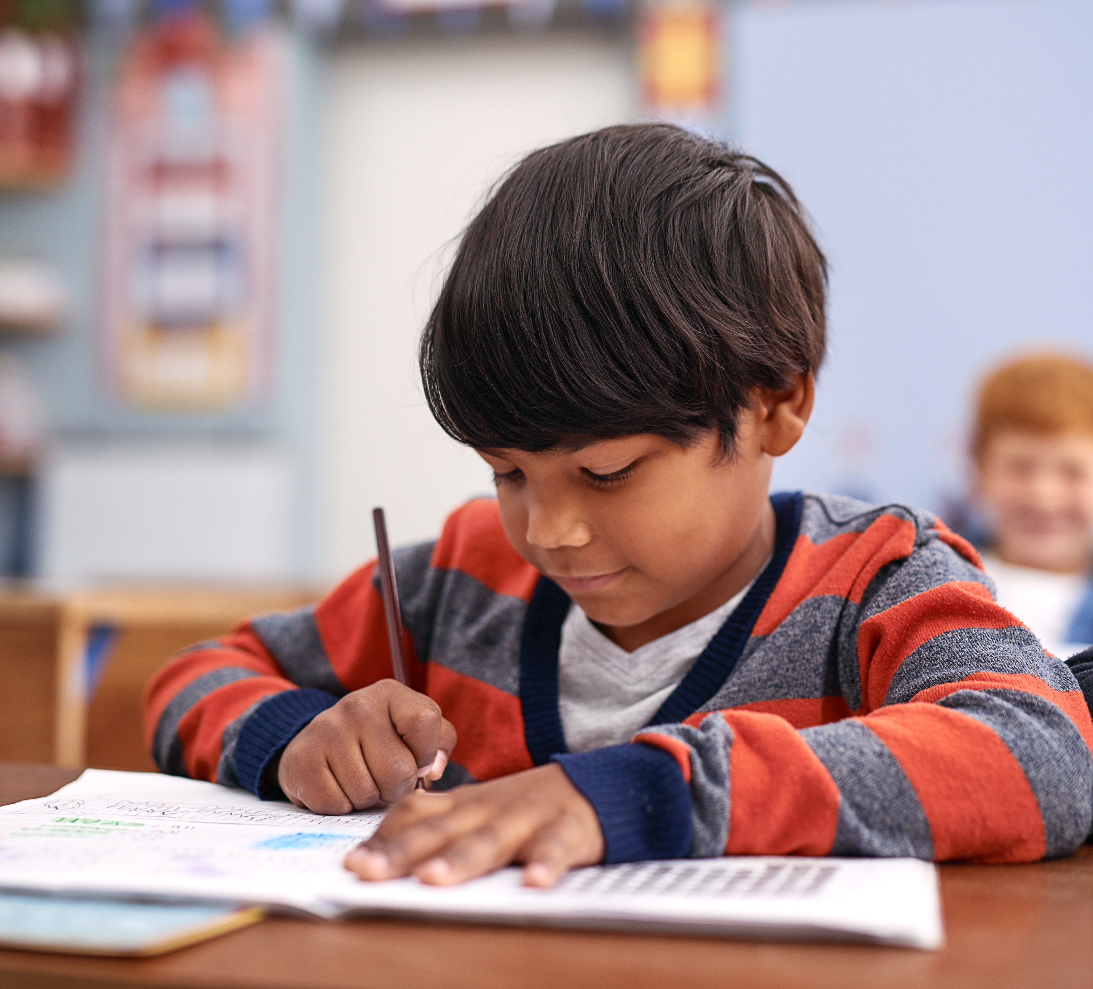 A young boy writing in a notebook while studying at a desk.