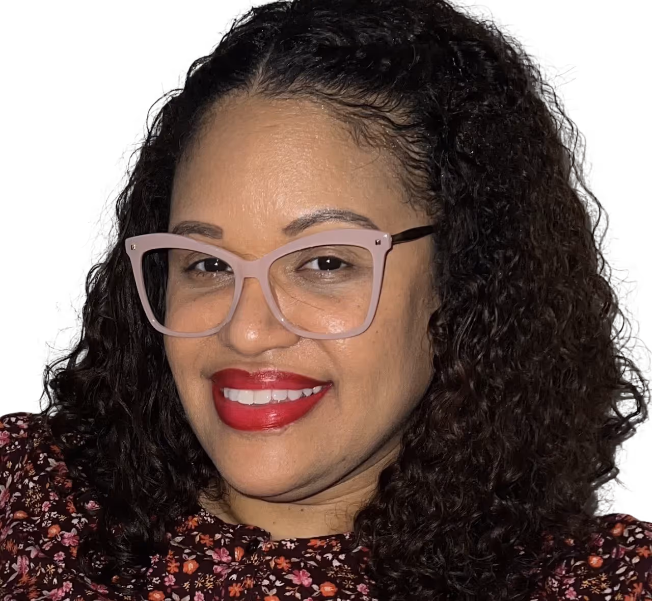 A smiling woman with curly hair and glasses, wearing a floral top and red lipstick