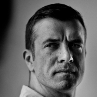 Black and white close-up portrait of a serious man with short dark hair looking slightly to the side.