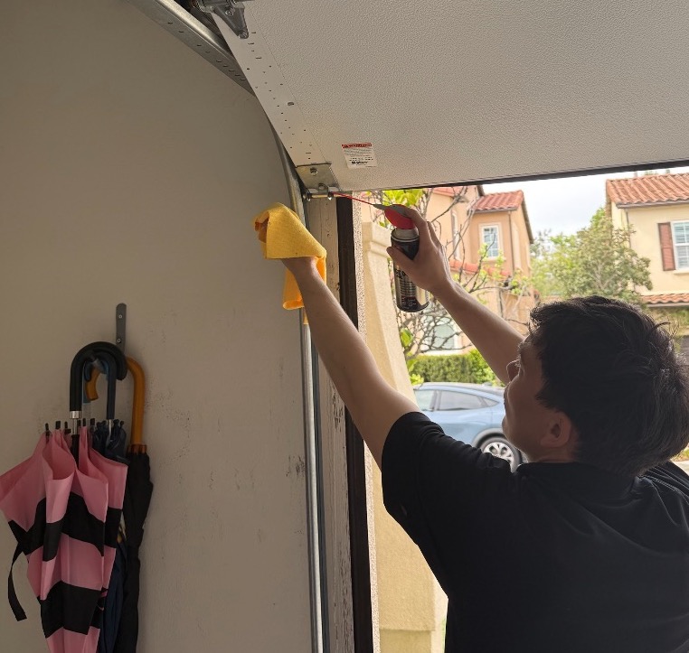 Livd handyman spraying lubricant on a garage door roller and hinge