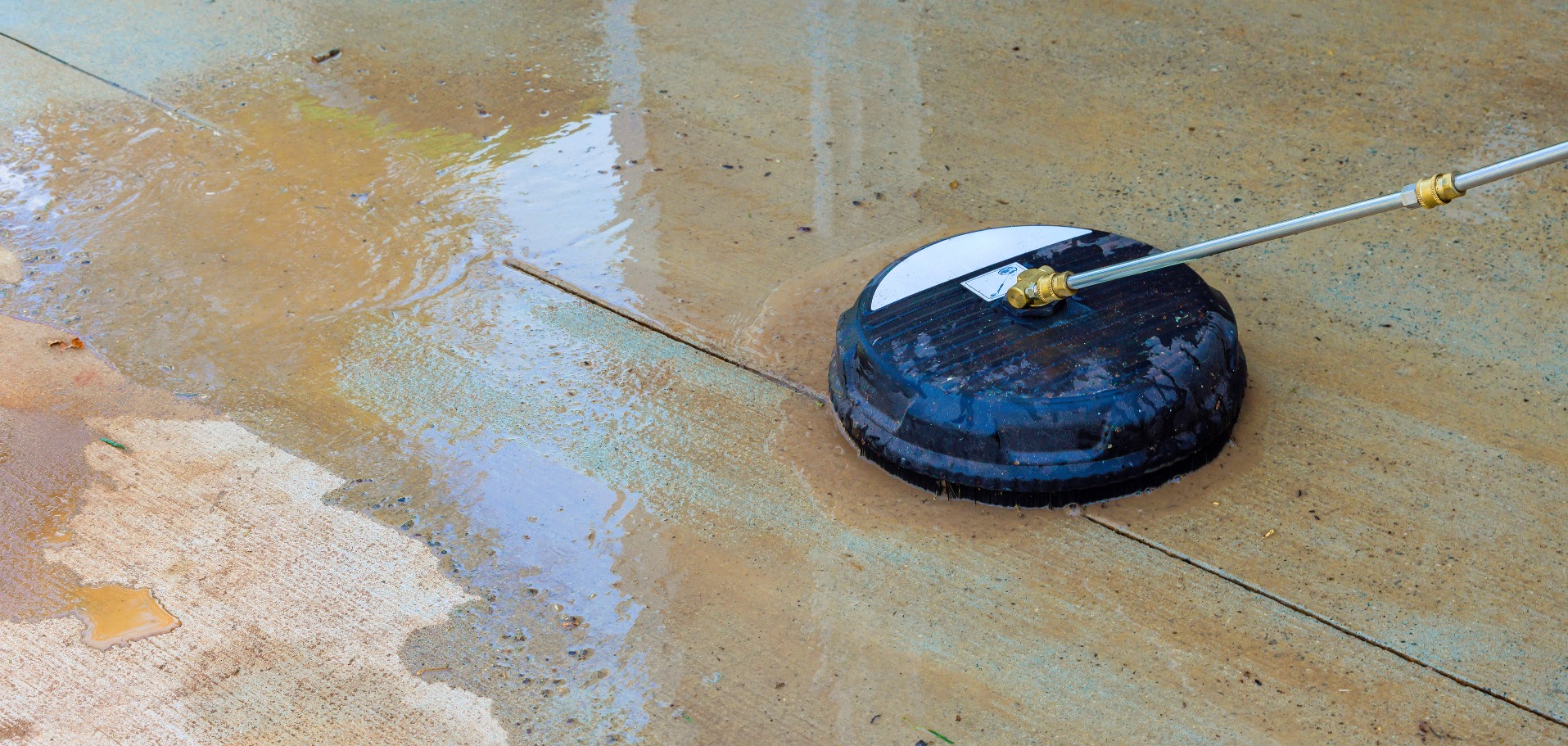 Pressure washer surface cleaner attachment cleaning a concrete patio, leaving a clean stripe on dirty concrete