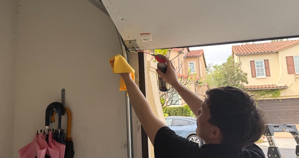 Livd handyman spraying lubricant on a garage door roller and hinge