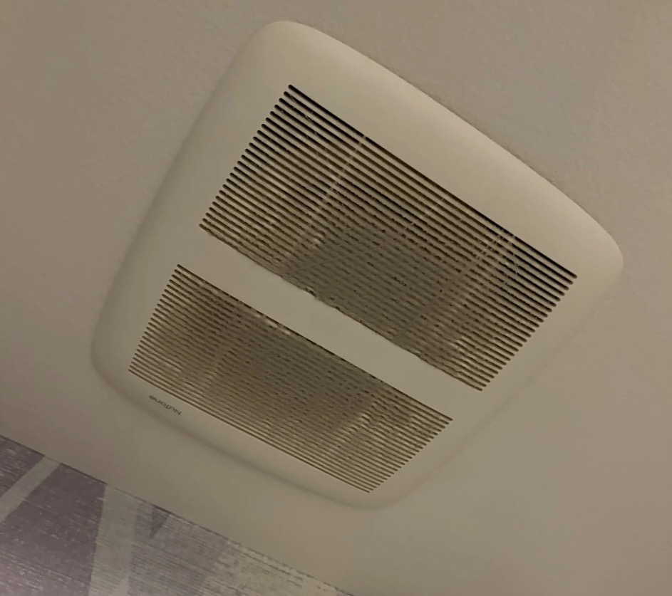 Dusty bathroom exhaust fan cover on a ceiling