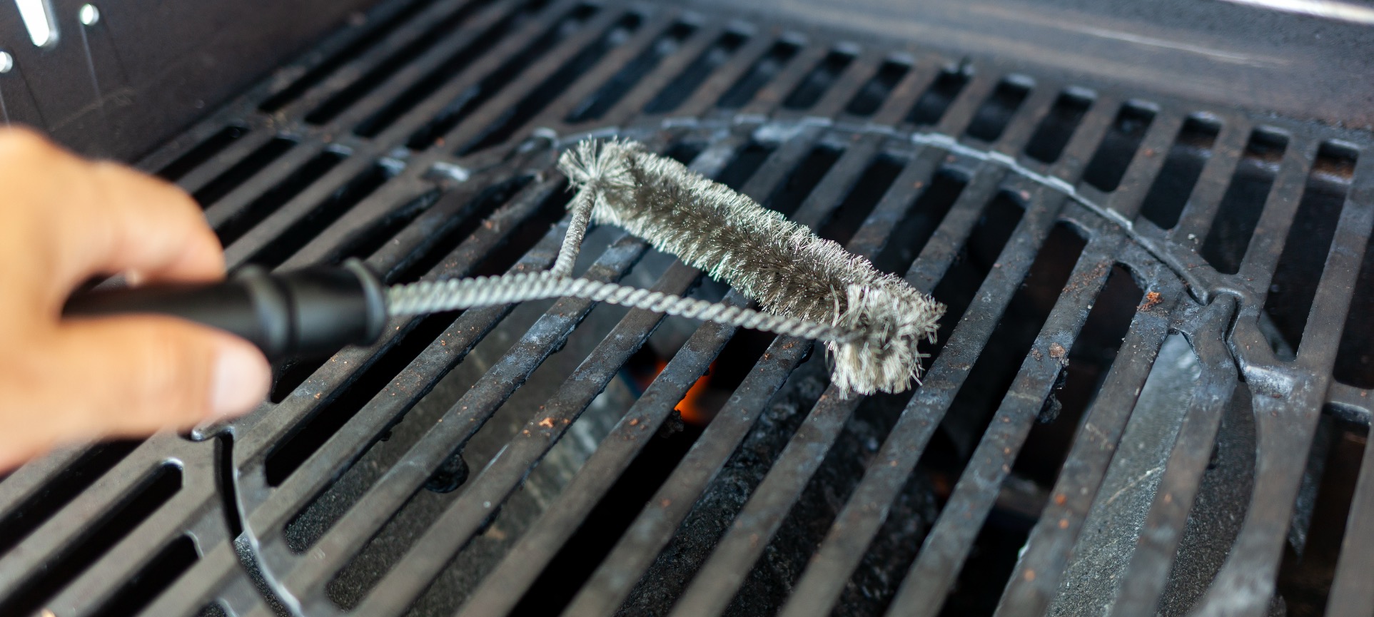 Grill brush scrubbing hot cast-iron grates on a gas BBQ grill