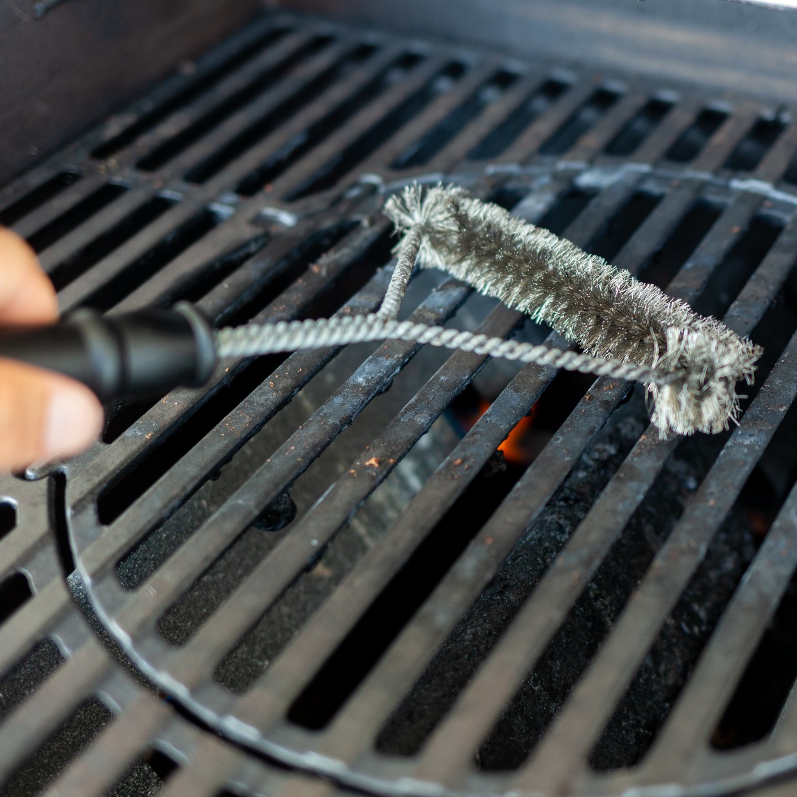 Grill brush scrubbing hot cast-iron grates on a gas BBQ grill
