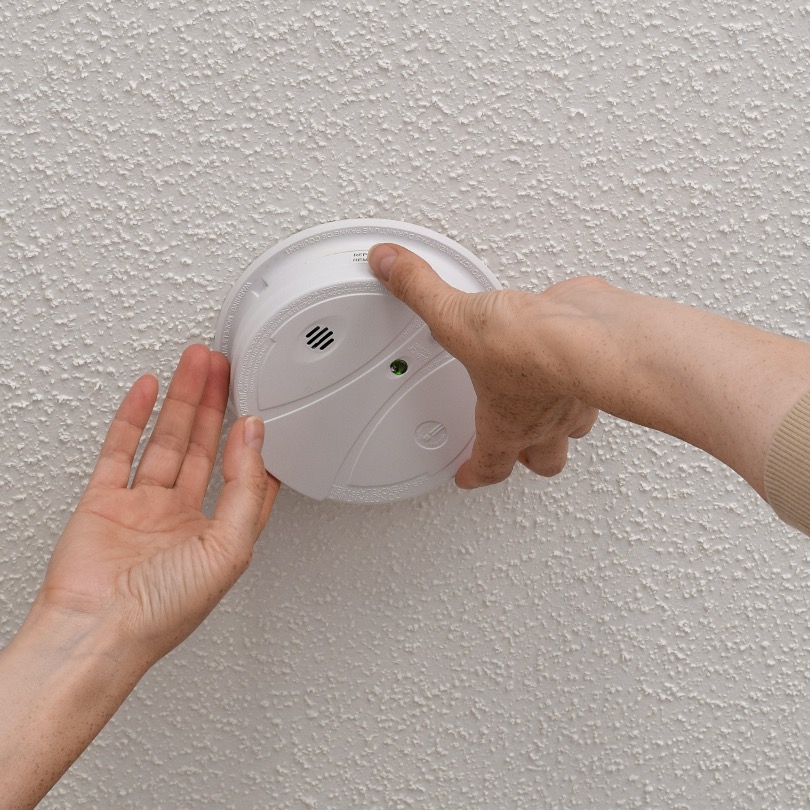 Homeowner removing a carbon monoxide detector from the ceiling to check it